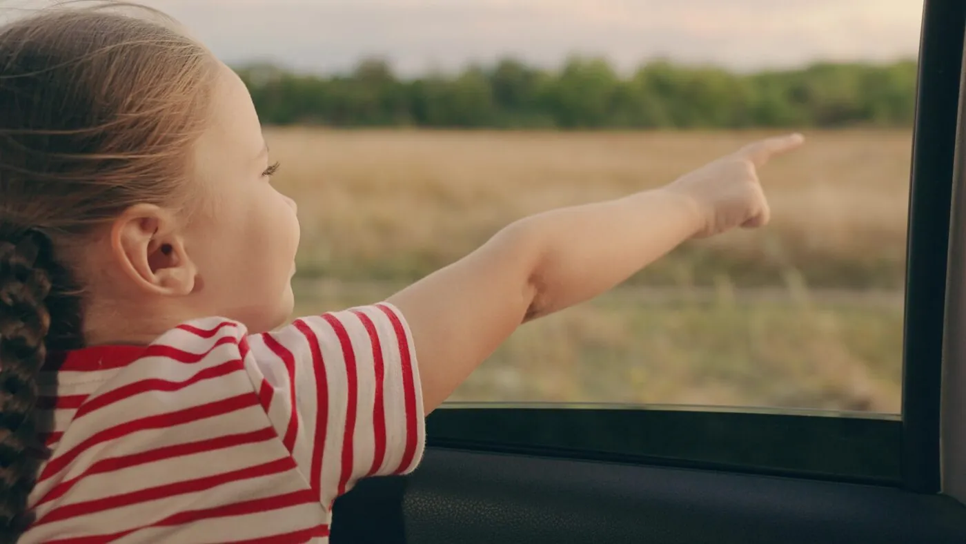 Kleines Mädchen zeigt auf die Landschaft aus dem Autofenster bei der Fahrt
