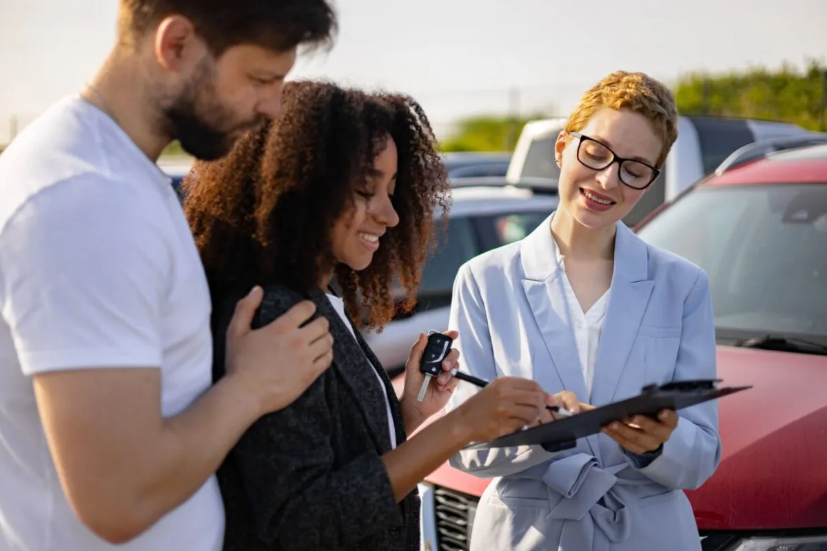 Paar erhält Autoschlüssel und Kaufvertrag von ihrer Serviceberaterin