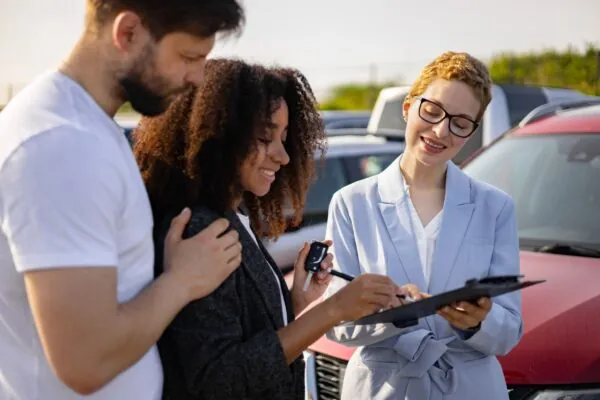 Paar erhält Autoschlüssel und Kaufvertrag von ihrer Serviceberaterin