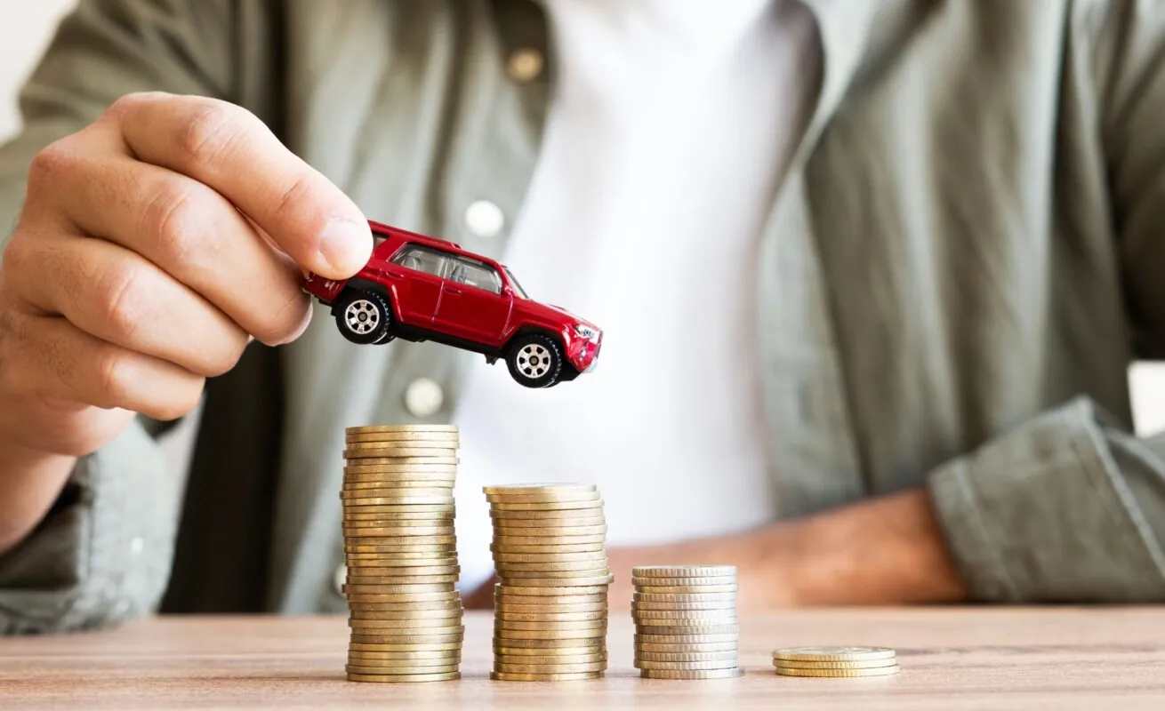 Mann platziert rotes Modellauto auf gestapelten Münzen